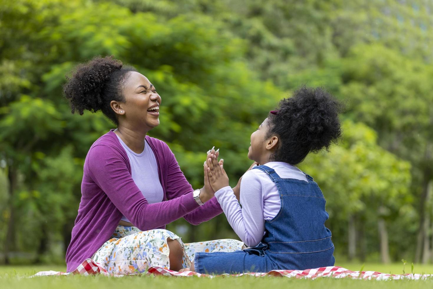 African American mother is laughing while playing patty cake with her young daughter while having a summer picnic in the public park for wellbeing and happiness concept photo