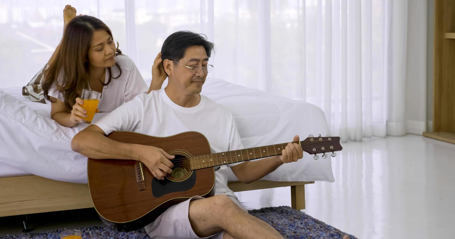 Happy asian lover playing guitar and singing songs together in a bedroom. photo