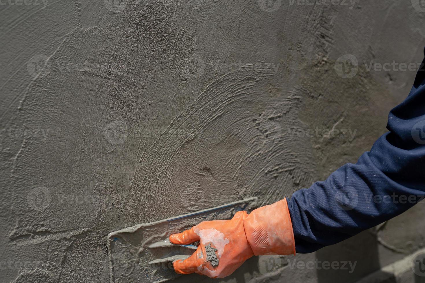 Close-up shot of a cement worker using a trowel to plaster cement in construction. photo