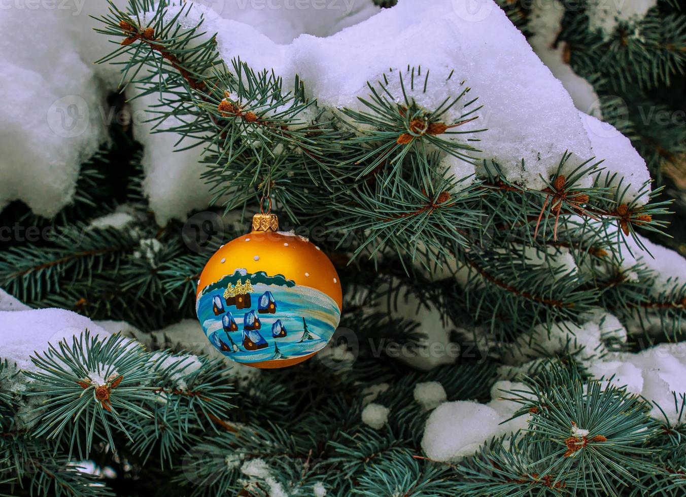 Christmas ball hanging on a snow-covered branch of a Christmas tree on a festive background of white snow and snowy bokeh with copy space. photo