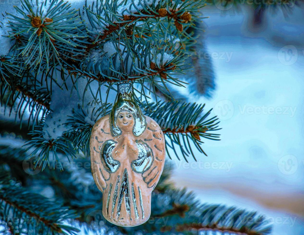 Christmas toy angel hangs on a snow-covered branch of a Christmas tree on a festive background of white snow bokeh with copy space. photo