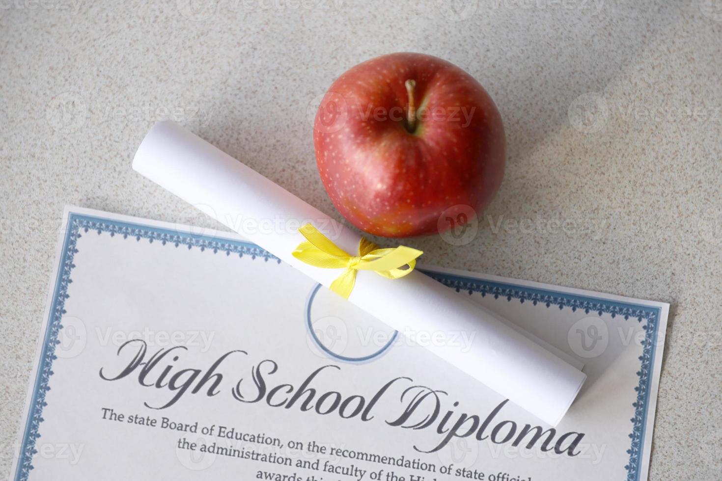 A high school diploma lies on table with small scroll and red apple. Education documents photo