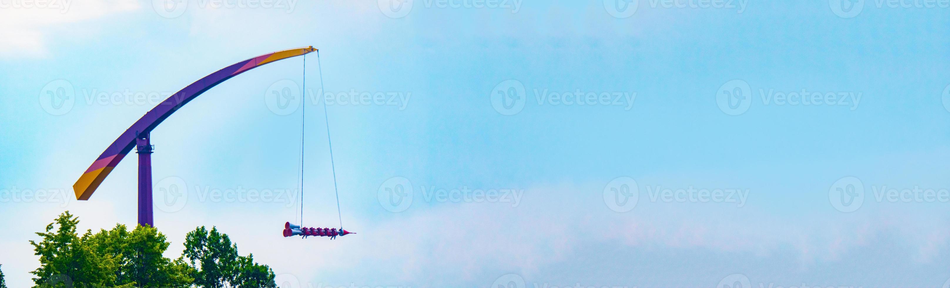 landscape of an amusement park with rocket rides attraction showing above the tree tops against a blue sky. photo