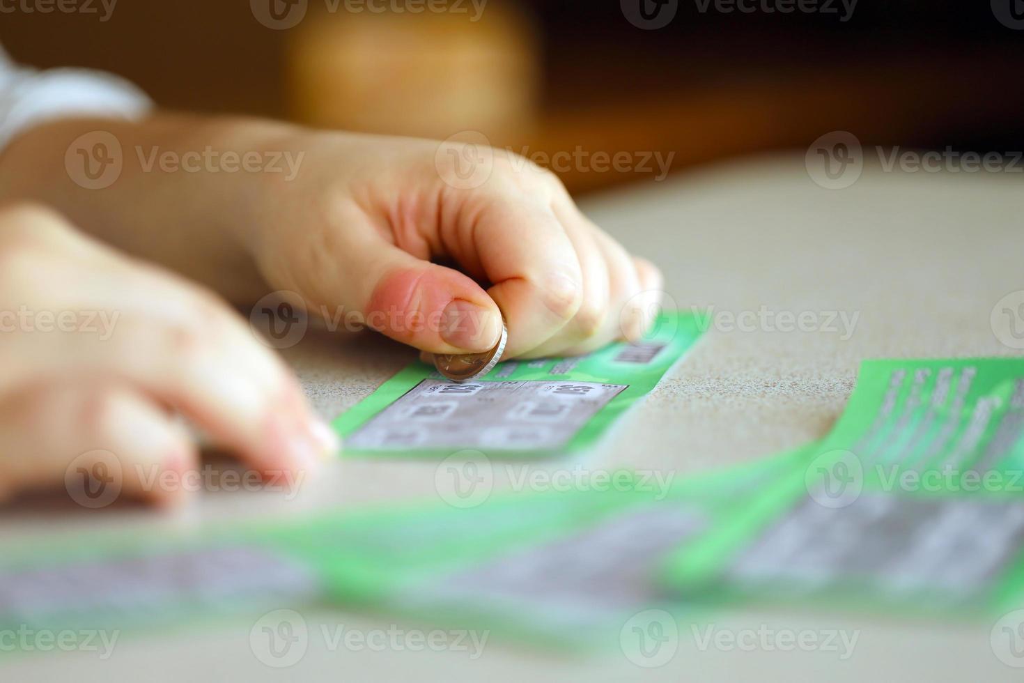 Close up view of silver coin in hand of gambler scratching fake lottery card. Lottery gambling concept, scratching cards lottery photo