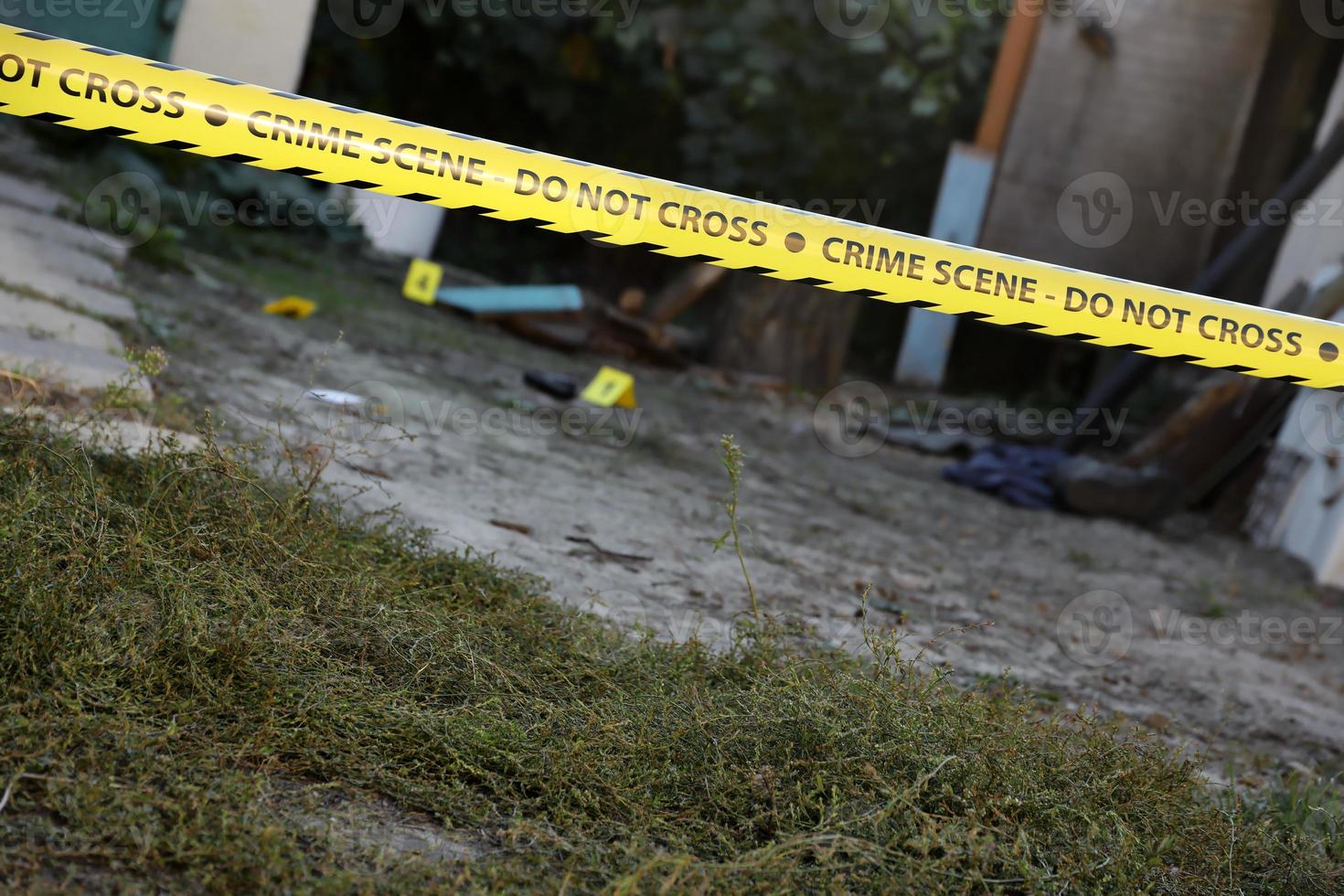 Victim of a violent crime in a backyard of residental house in evening. Dead man body under the yellow police line tape and evidence markers on crime scene photo