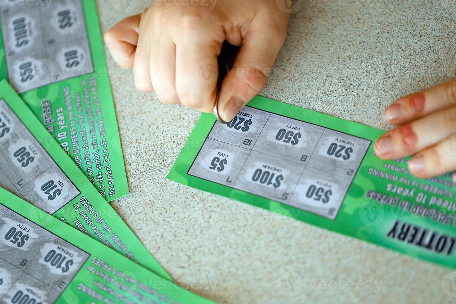 Close up view of silver coin in hand of gambler scratching fake lottery card. Lottery gambling concept, scratching cards lottery photo