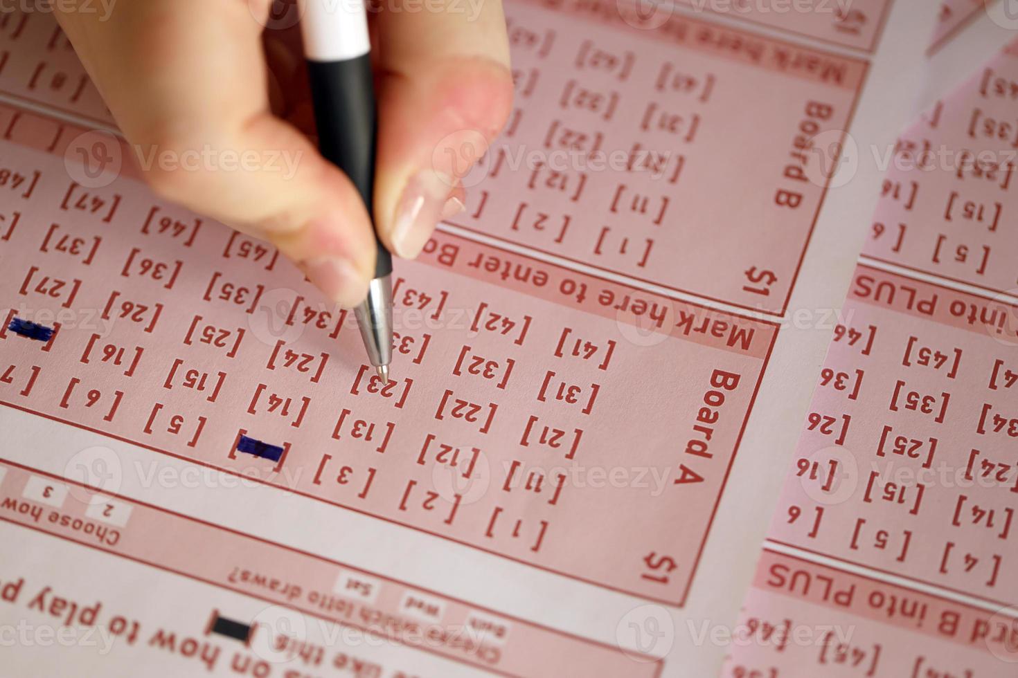 llenando un boleto de lotería. una joven juega a la lotería y sueña con ganar el premio mayor. mano femenina marcando el número en el billete de lotería rojo foto