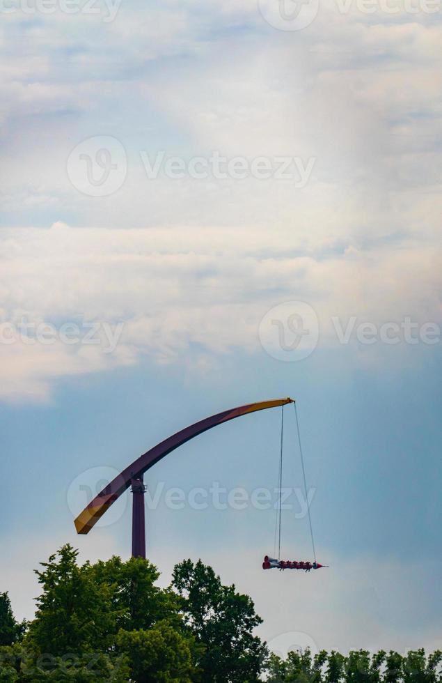 landscape of an amusement park with rocket rides attraction showing above the tree tops against a blue sky. photo