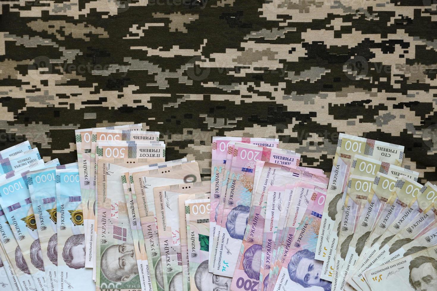 Ukrainian hryvnya bills on fabric with texture of Ukrainian military pixeled camouflage. Cloth with camo pattern in grey, brown and green pixel shapes photo