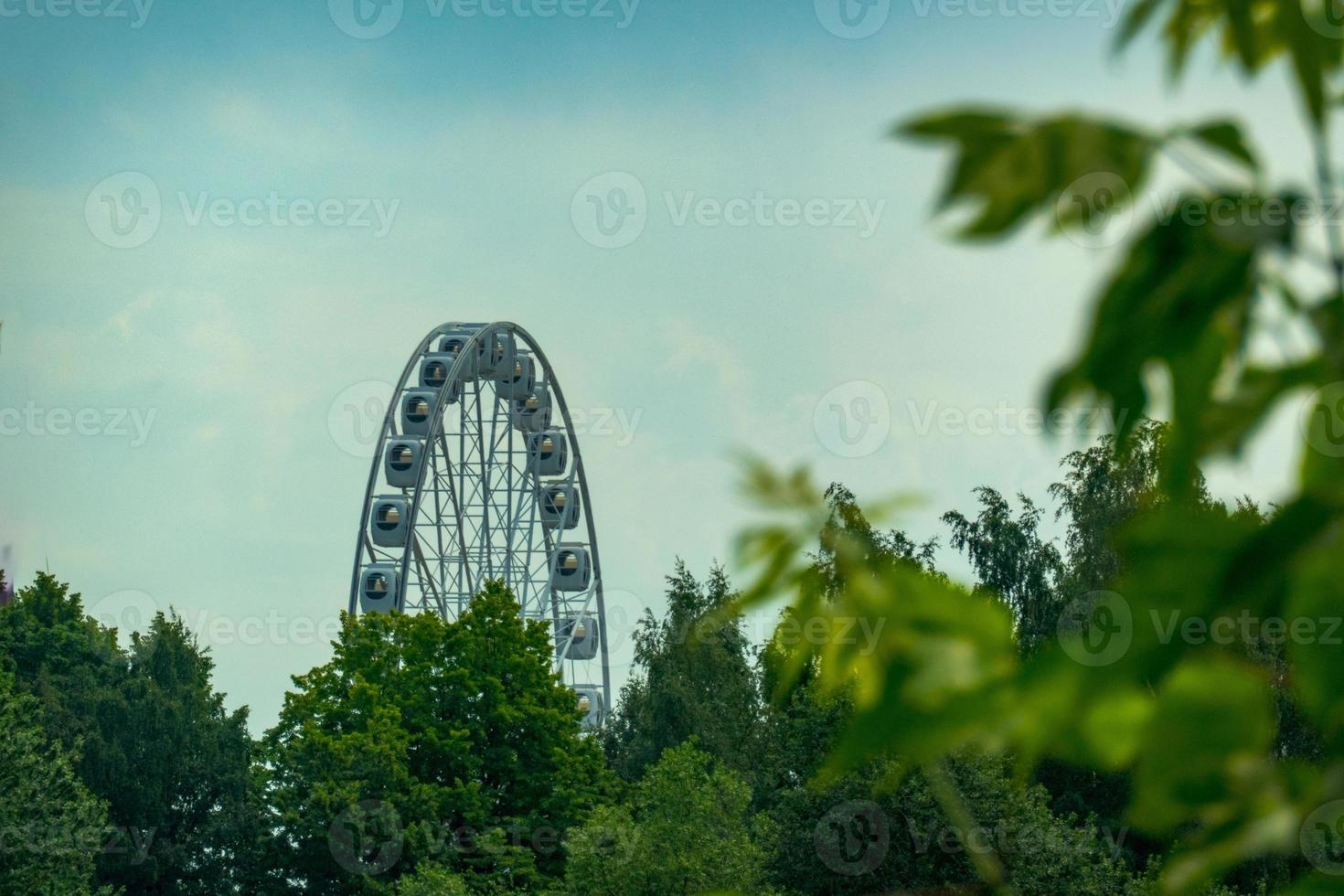 landscape of an amusement park with the top of a Ferris wheel showing above the tree tops against a blue sky. photo