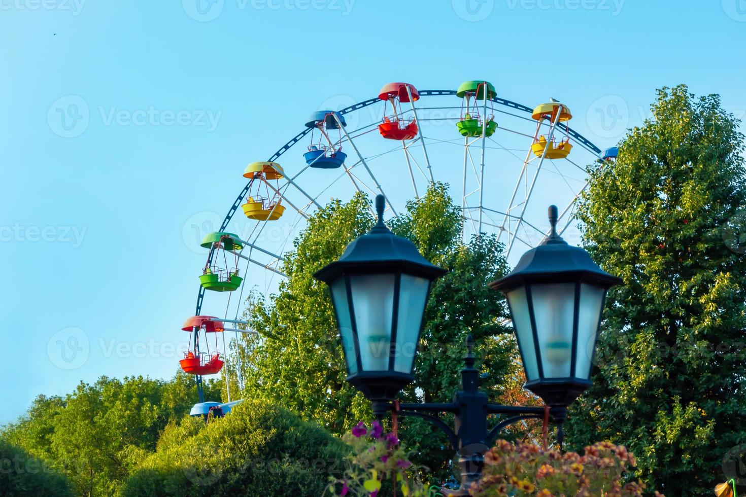 landscape of an amusement park with lantern decorated with flowers background the top of a Ferris wheel showing above the tree tops against a sky. photo