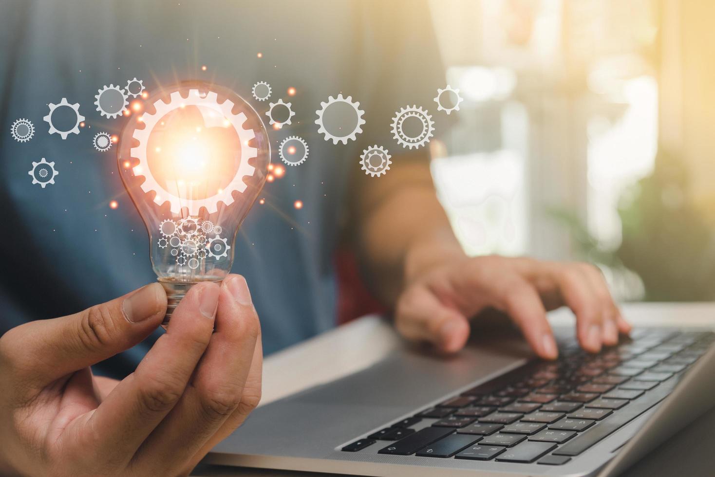 Man hand holding lightbulb and a gear icon a notebook computer. using online technology as a source of inspiration a fresh technology innovation concept. photo