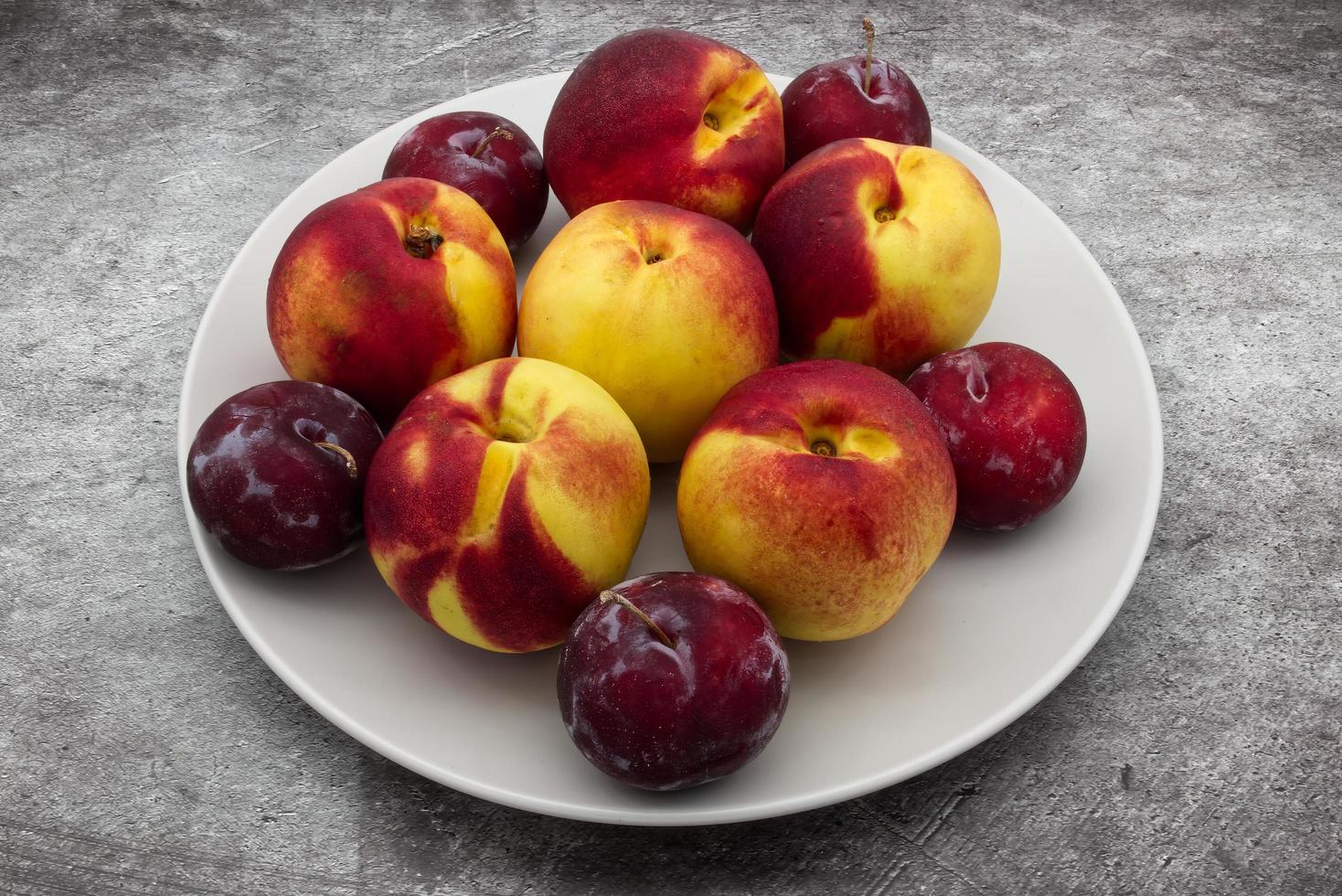 Plums and Peaches in a clear dish isolated on granite background photo
