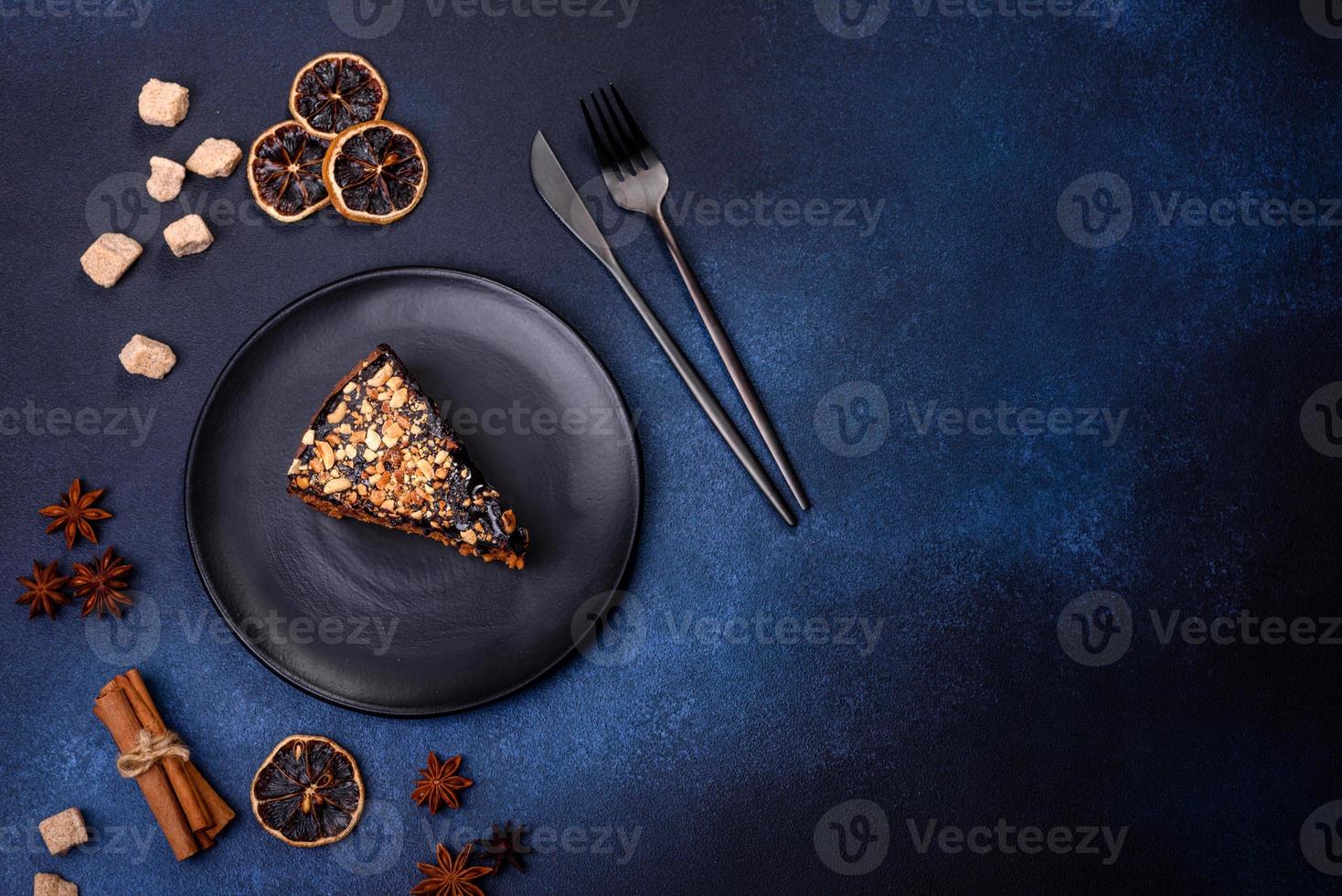 A piece of fresh delicious cake with nuts and chocolate on a black plate against a dark blue background photo