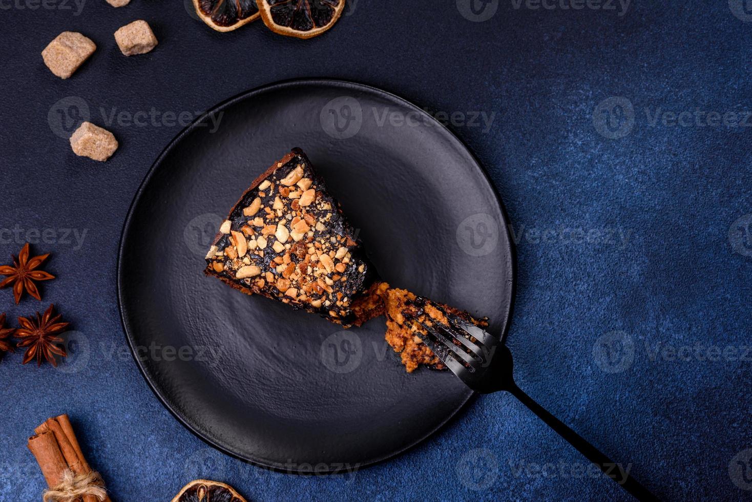 A piece of fresh delicious cake with nuts and chocolate on a black plate against a dark blue background photo