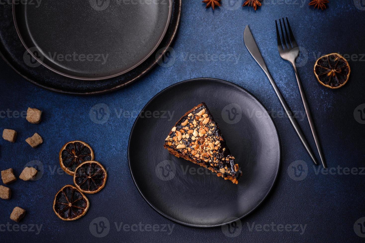 A piece of fresh delicious cake with nuts and chocolate on a black plate against a dark blue background photo