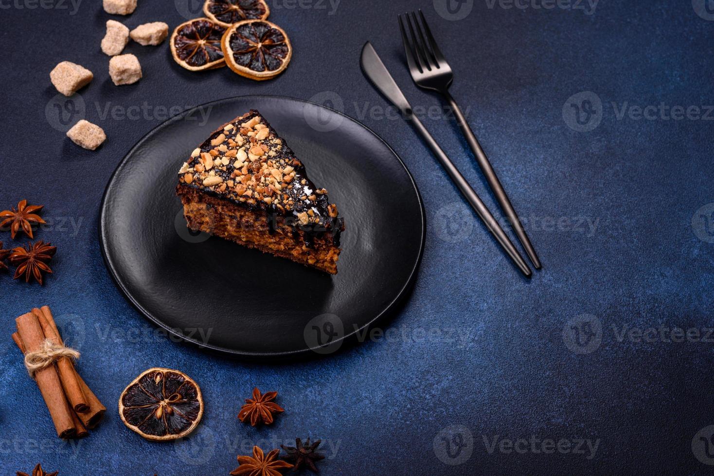 A piece of fresh delicious cake with nuts and chocolate on a black plate against a dark blue background photo