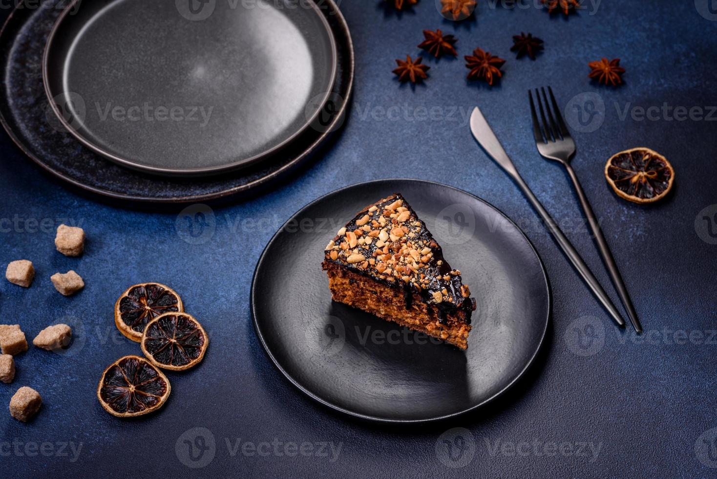 A piece of fresh delicious cake with nuts and chocolate on a black plate against a dark blue background photo