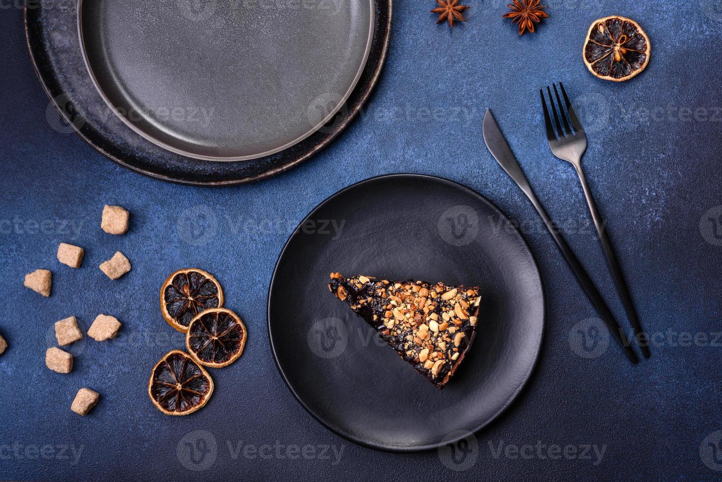 A piece of fresh delicious cake with nuts and chocolate on a black plate against a dark blue background photo