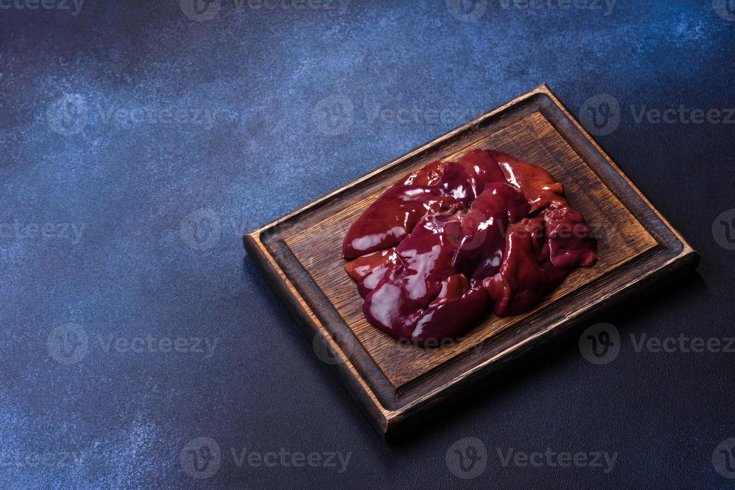 Pieces of raw liver on a wooden cutting board against a dark concrete background photo