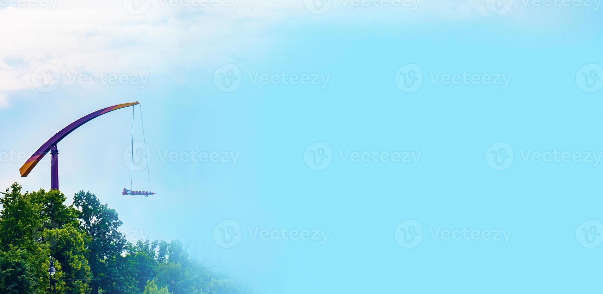 landscape of an amusement park with rocket rides attraction showing above the tree tops against a blue sky. photo