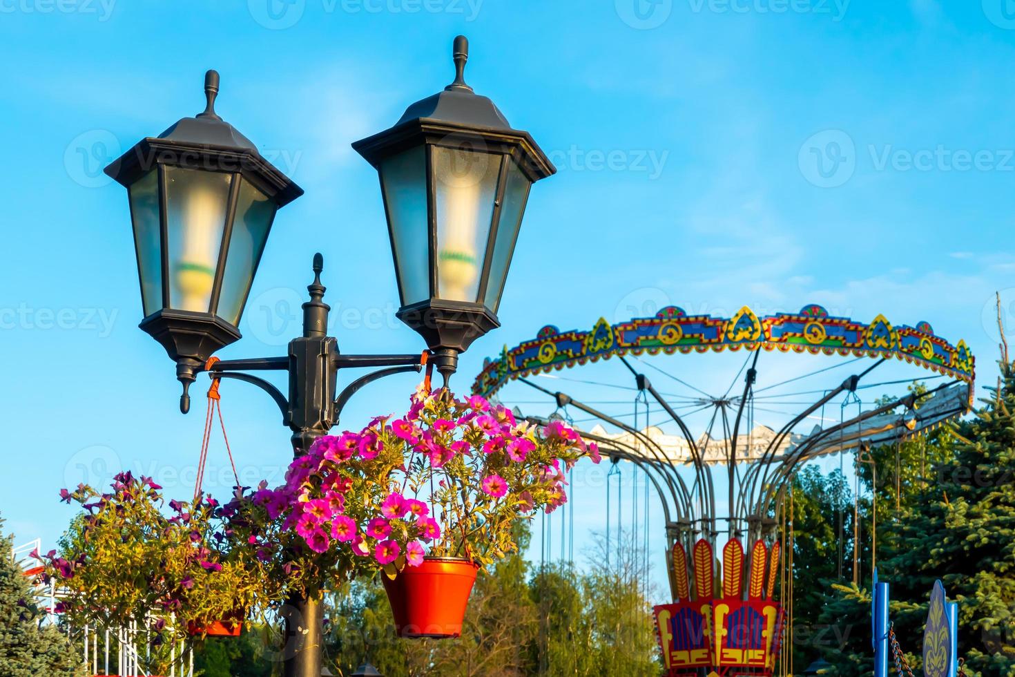 paisaje de un parque de diversiones con farolillos decorados con flores de fondo la parte superior de una noria que se muestra sobre las copas de los árboles contra un cielo. foto