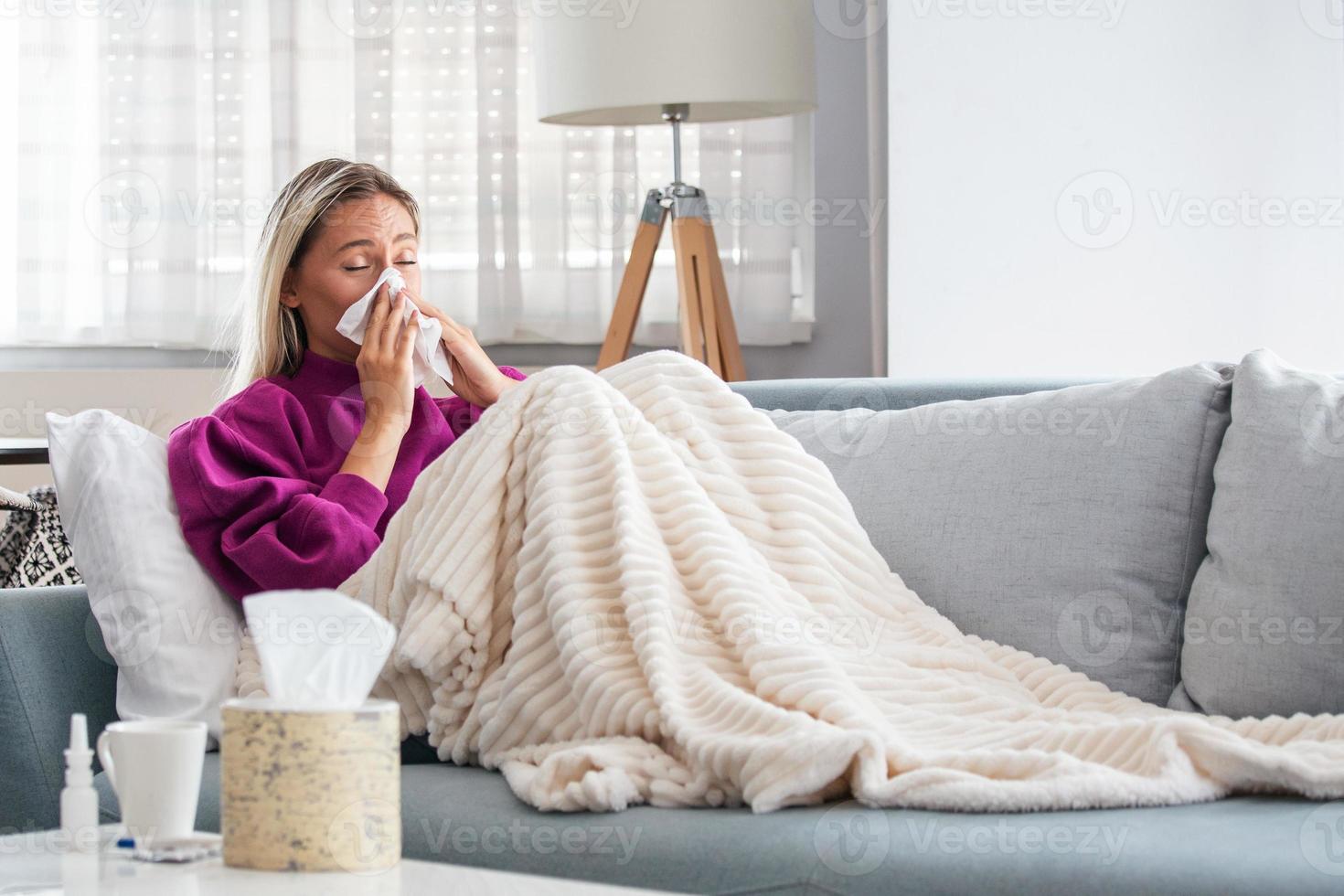 Sick woman with headache sitting under the blanket. Sick woman with seasonal infections, flu, allergy lying in bed. Sick woman covered with a blanket lying in bed with high fever and a flu, resting. photo