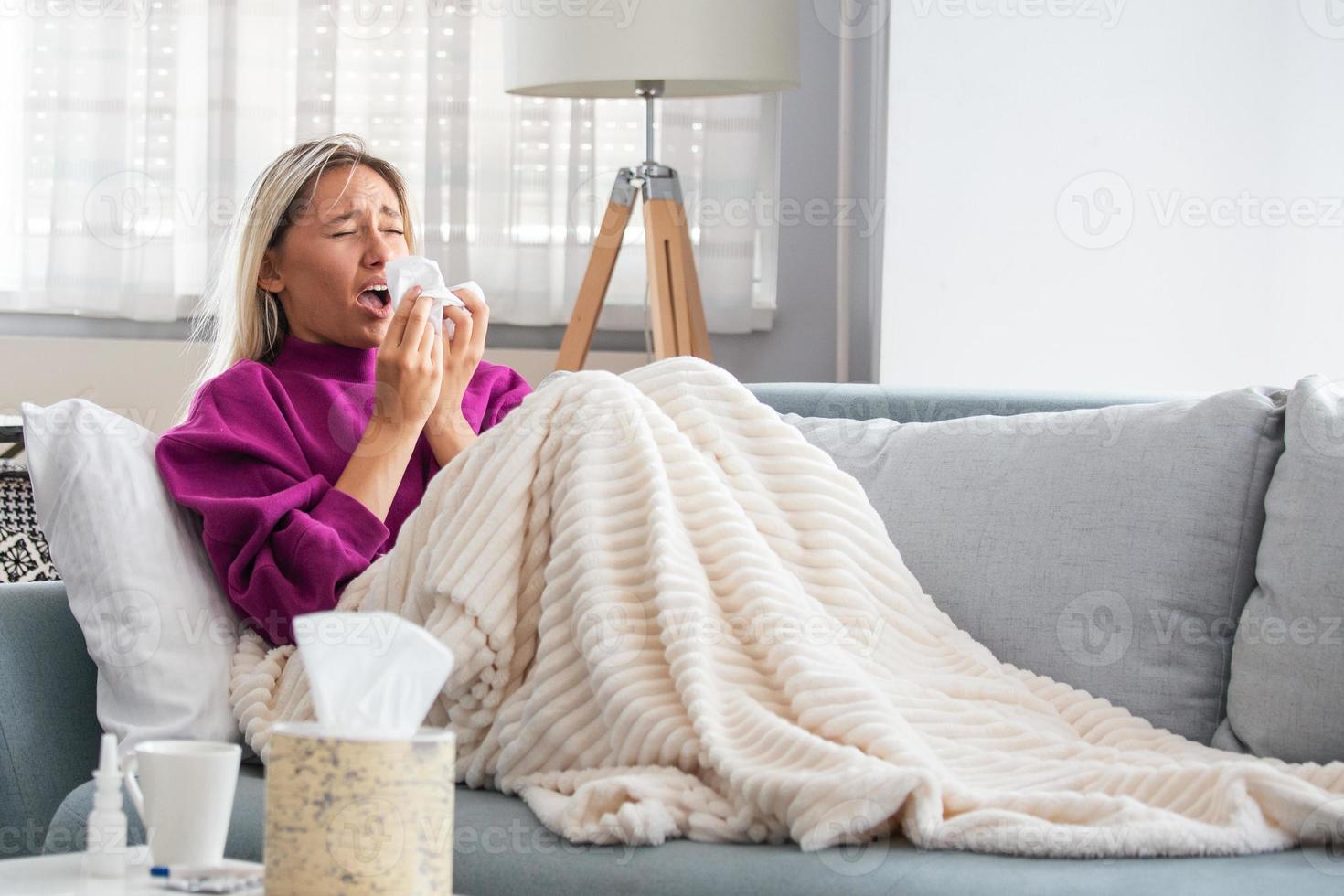 Sick Woman.Flu.Woman Caught Cold. Sneezing into Tissue. Headache. Virus .Medicines. Young Woman Infected With Cold Blowing Her Nose In Handkerchief. Sick woman with a headache sitting on a sofa photo