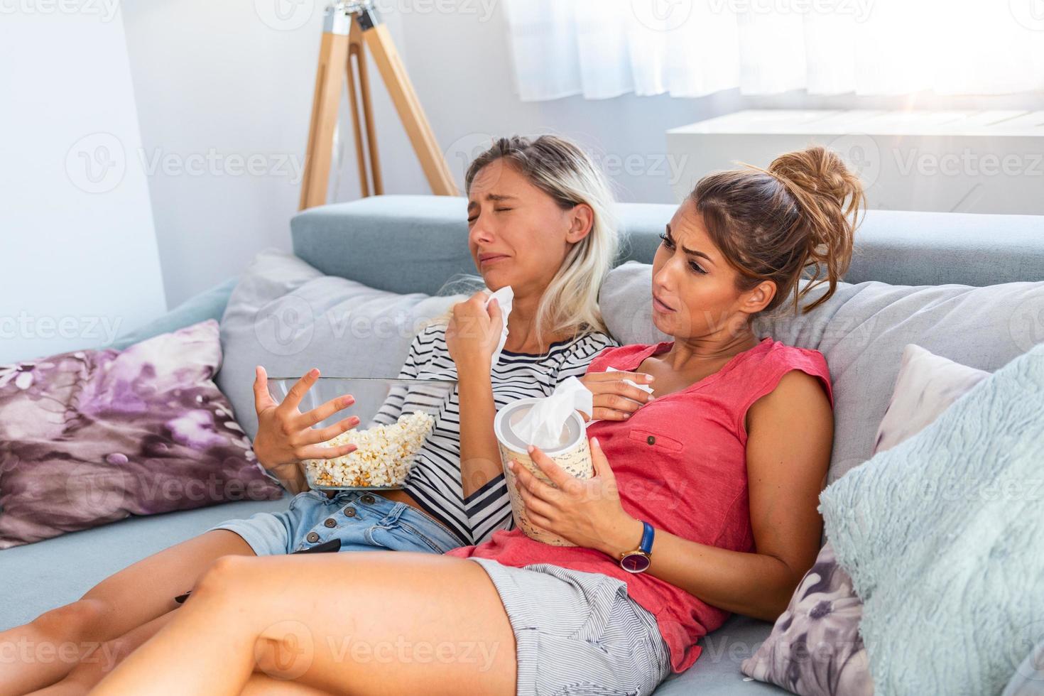 Two sad friends crying watching tv in the night sitting on a couch in the living room at home. Pretty girls watching sad movie photo