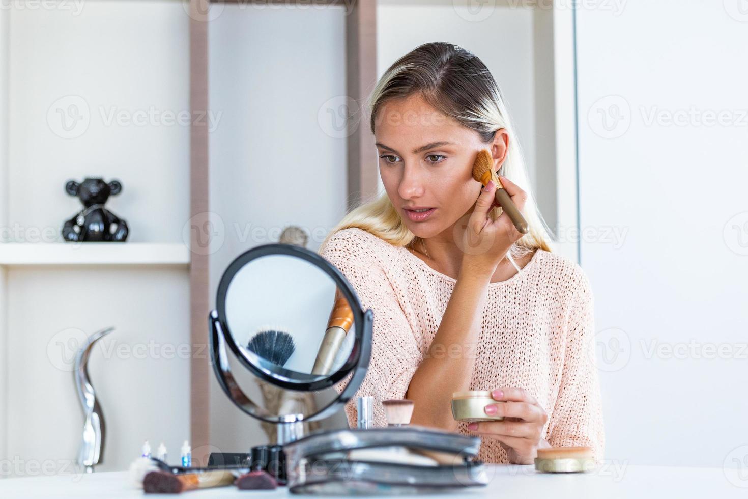 Beauty woman applying makeup. Beautiful girl looking in the mirror and applying cosmetic with a big brush. Girl gets blush on the cheekbones. Powder, rouge photo