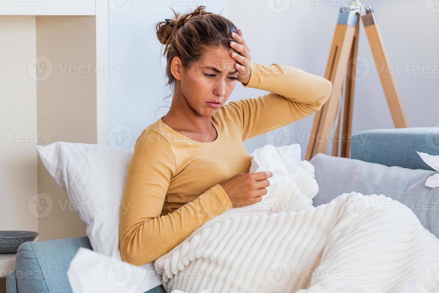 Sick woman with headache sitting under the blanket. Sick woman with seasonal infections, flu, allergy lying in bed. Sick woman covered with a blanket lying in bed with high fever and a flu, resting. photo