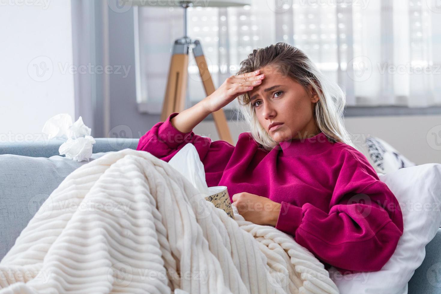 Sick woman with headache sitting under the blanket. Sick woman with seasonal infections, flu, allergy lying in bed. Sick woman covered with a blanket lying in bed with high fever and a flu, resting. photo