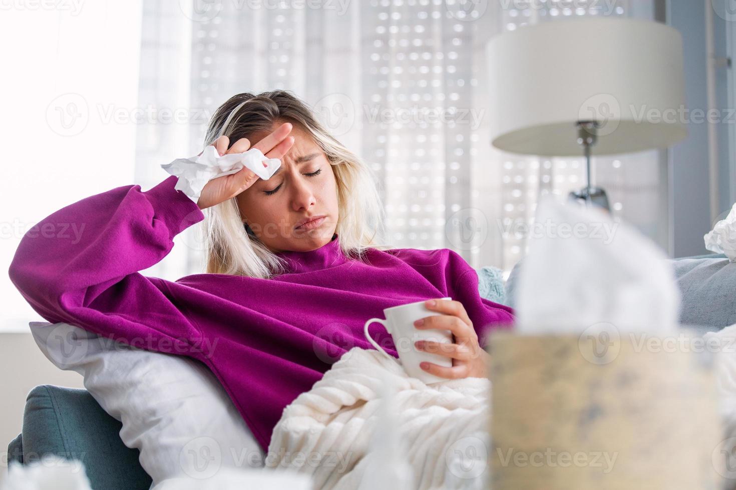 Sick Woman.Flu.Woman Caught Cold. Sneezing into Tissue. Headache. Virus .Medicines. Young Woman Infected With Cold Blowing Her Nose In Handkerchief. Sick woman with a headache sitting on a sofa photo