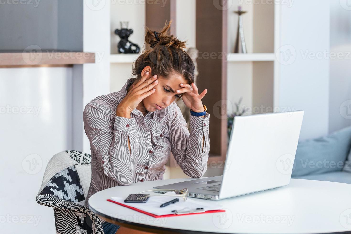 Young frustrated woman working at office desk in front of laptop suffering from chronic daily headaches, treatment online, appointing to a medical consultation, electromagnetic radiation, sick pay photo
