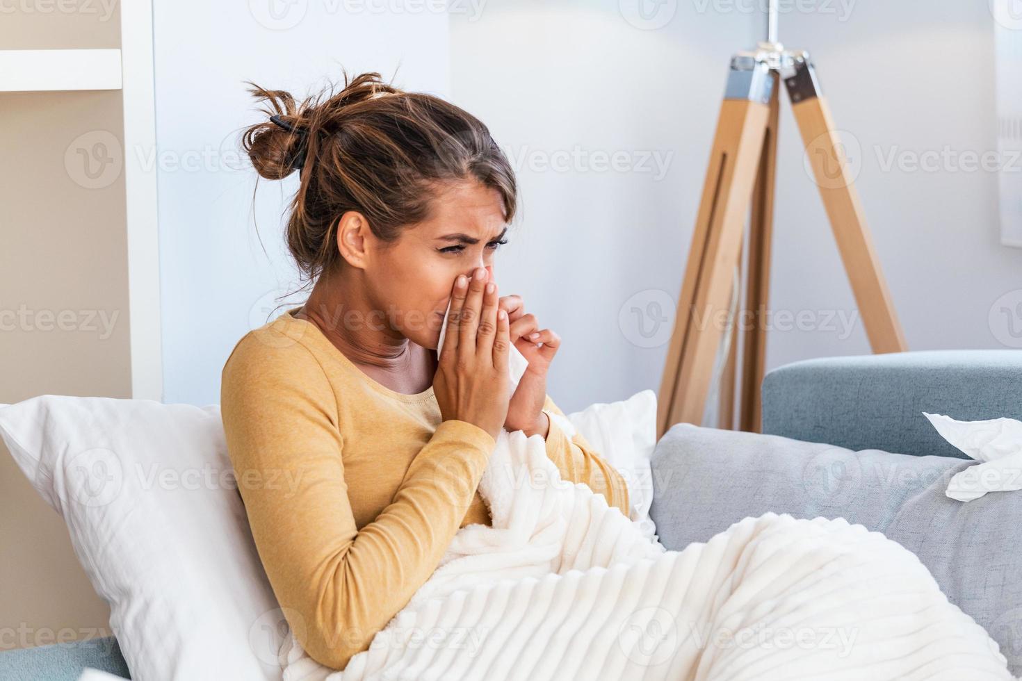 Sick Woman.Flu.Woman Caught Cold. Sneezing into Tissue. Headache. Virus .Medicines. Young Woman Infected With Cold Blowing Her Nose In Handkerchief. Sick woman with a headache sitting on a sofa photo