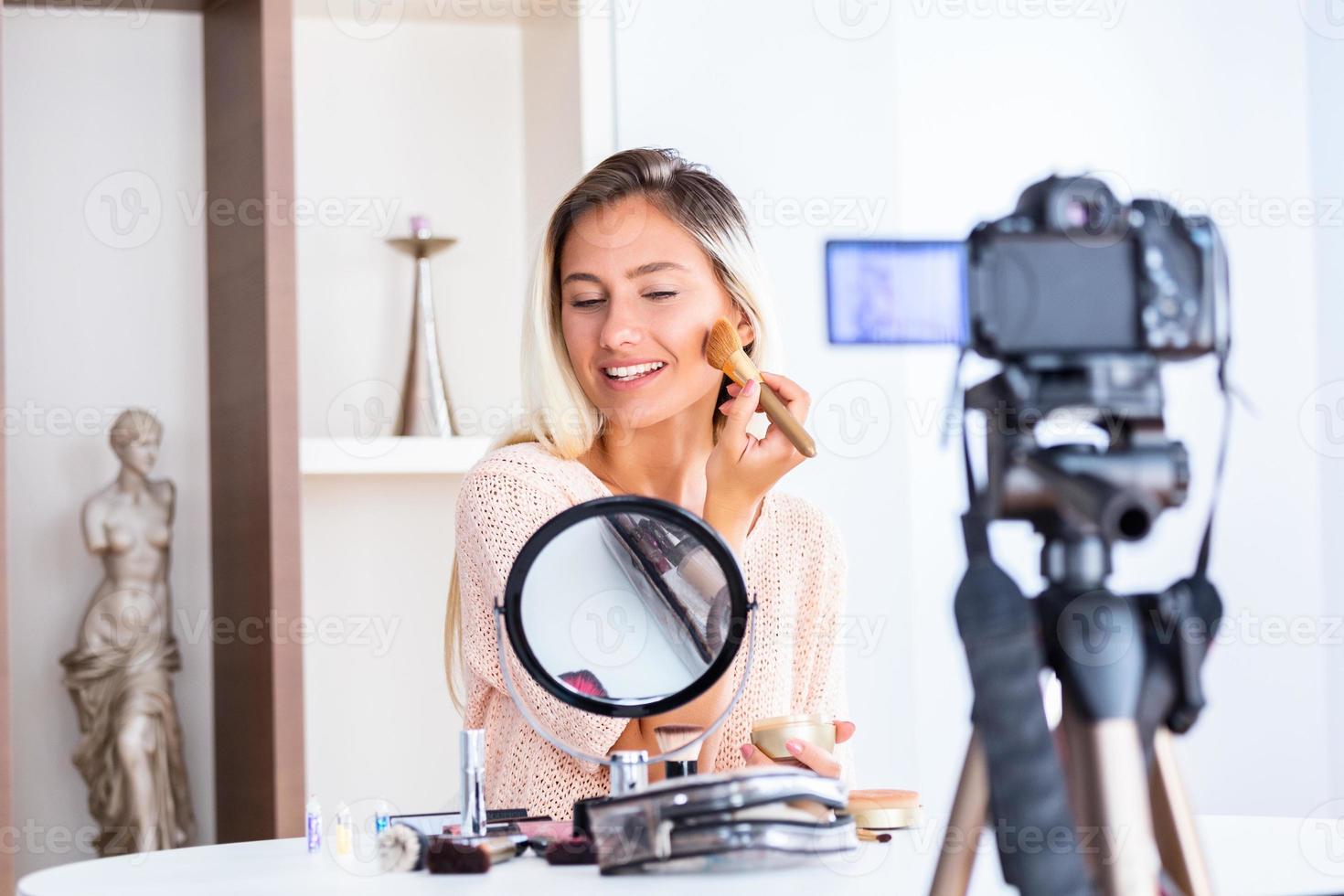 Famous blogger. Cheerful female vlogger is showing cosmetics products while recording video and giving advices for her beauty blog. Focus on digital camera photo