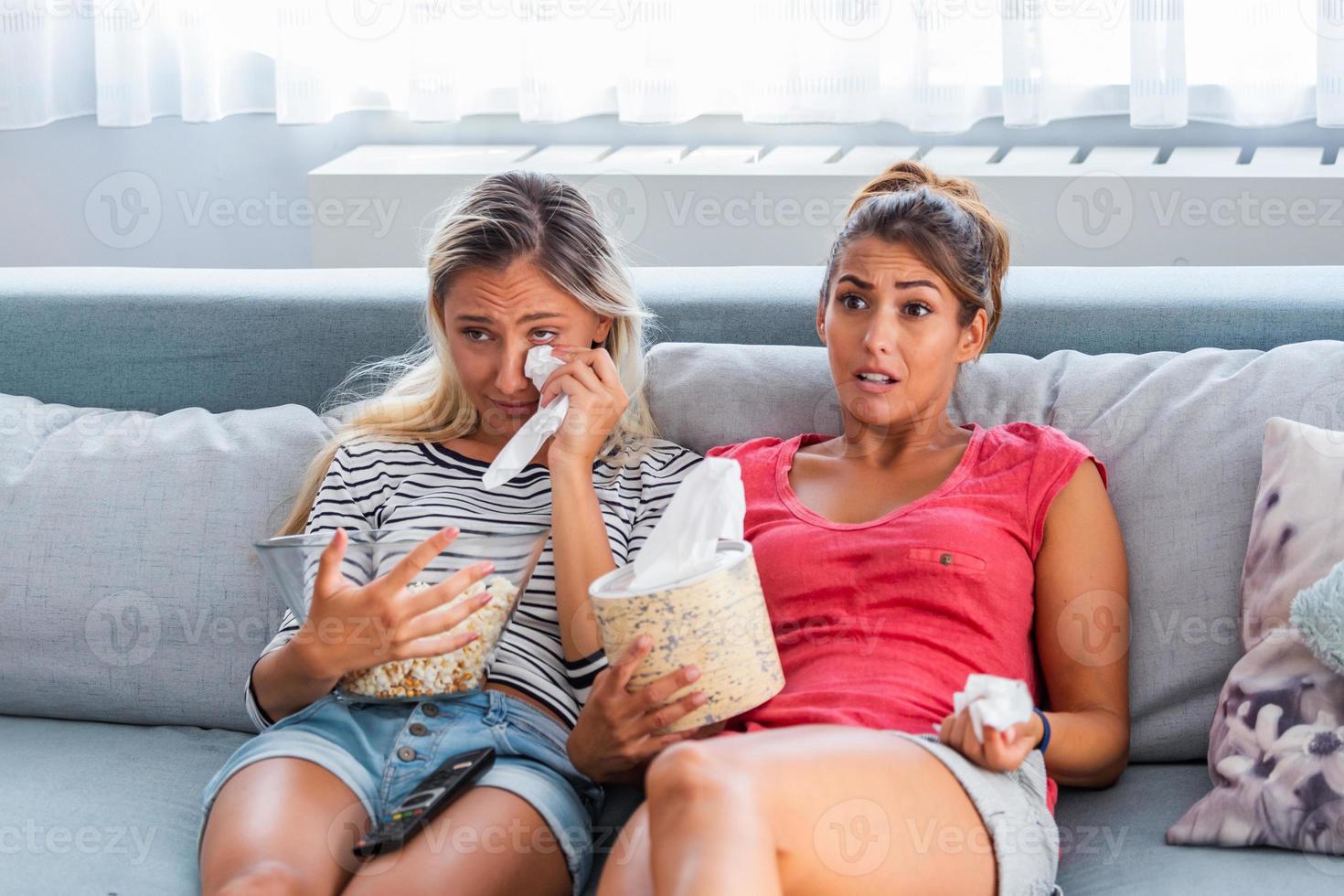 dos amigas sentimentales molestan llorando y limpiando lágrimas con pañuelos mientras ven una película dramática y triste, un programa de televisión o tocan un viejo video casero en una laptop mientras se sientan en un sofá en casa foto