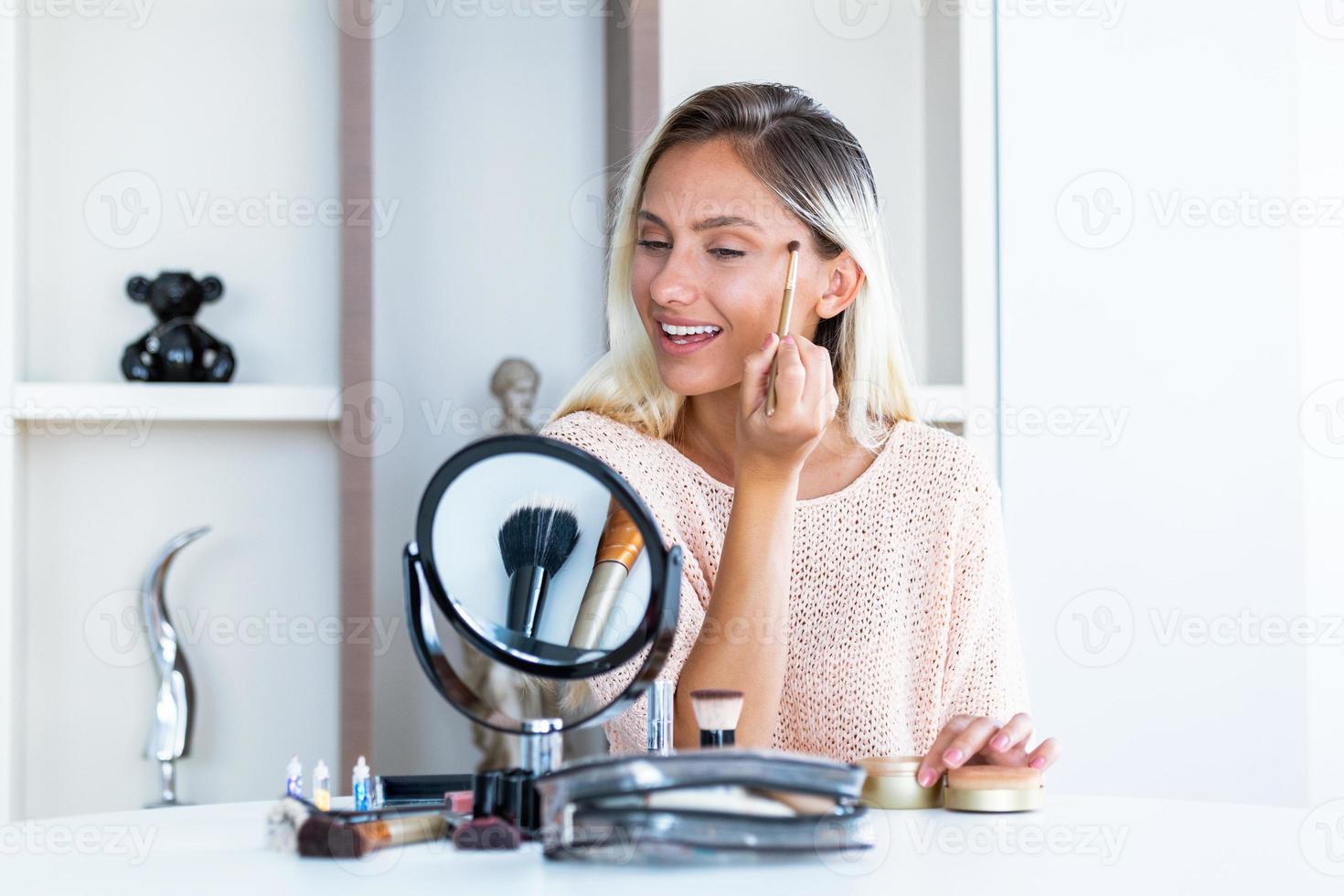 Beauty woman applying makeup. Beautiful girl looking in the mirror and applying cosmetic with a big brush. Girl gets blush on the cheekbones. Powder, rouge photo