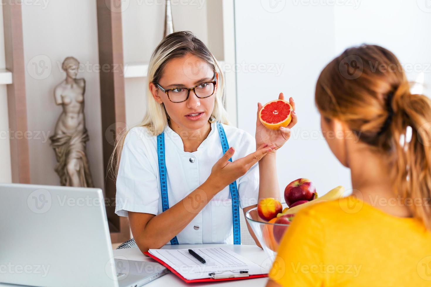 Portrait of young smiling female nutritionist in the consultation room. Making diet plan. Young woman visiting nutritionist in weight loss clinic photo