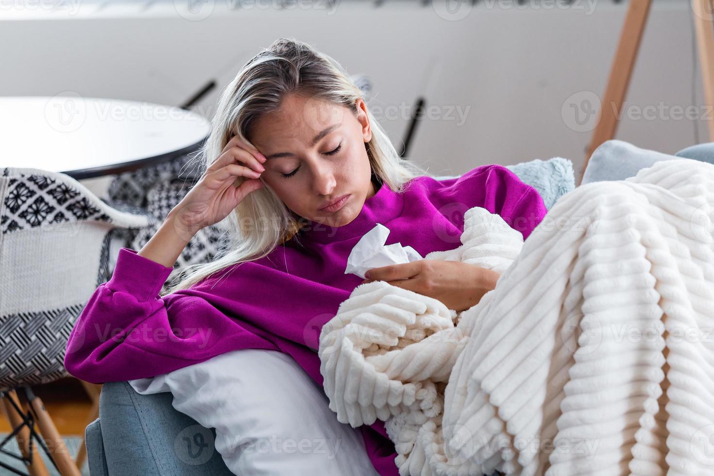 Sick woman with headache sitting under the blanket. Sick woman with seasonal infections, flu, allergy lying in bed. Sick woman covered with a blanket lying in bed with high fever and a flu, resting. photo