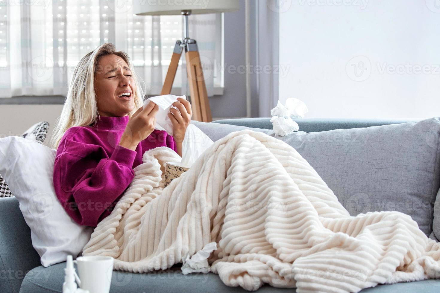 Sick desperate woman has flu. Rhinitis, cold, sickness, allergy concept. Pretty sick woman has runnning nose, rubs nose with handkerchief. Sneezing female. Brunette sneezing in a tissue photo