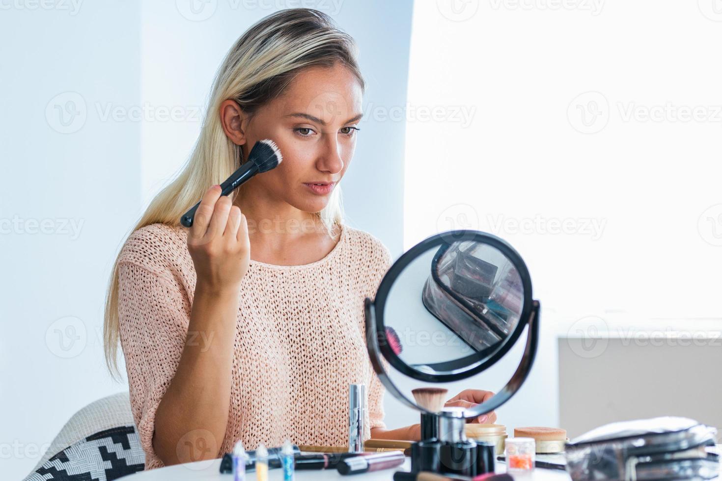 Beauty woman applying makeup. Beautiful girl looking in the mirror and applying cosmetic with a big brush. Girl gets blush on the cheekbones. Powder, rouge photo