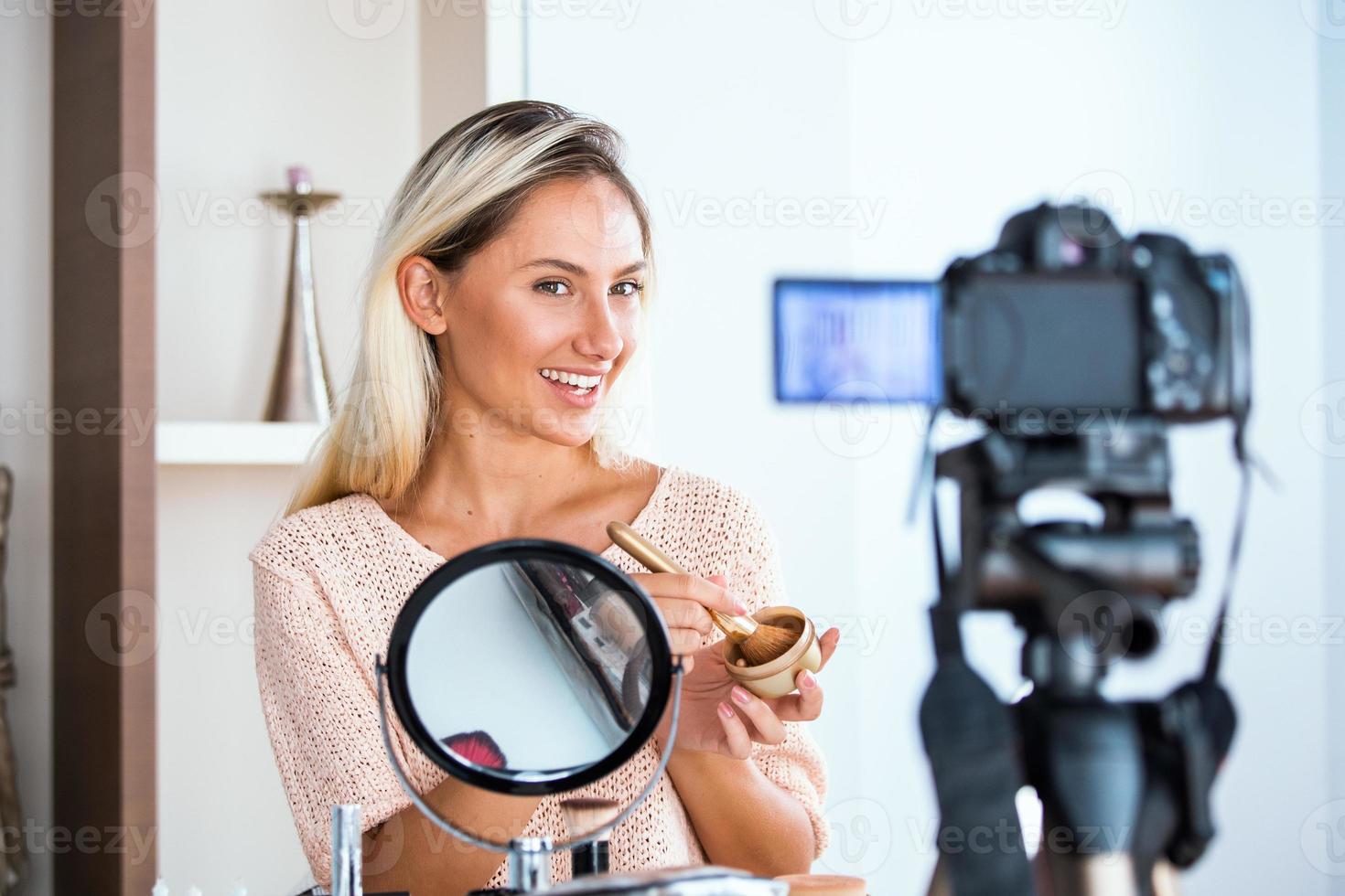 Famous blogger. Cheerful female vlogger is showing cosmetics products while recording video and giving advices for her beauty blog. Focus on digital camera photo