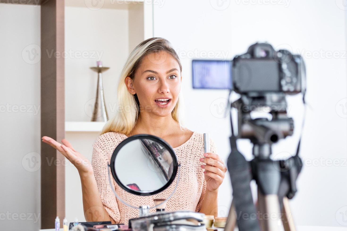 Famous blogger. Cheerful female vlogger is showing cosmetics products while recording video and giving advices for her beauty blog. Focus on digital camera photo