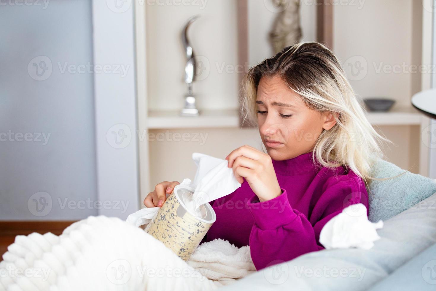 Sick desperate woman has flu. Rhinitis, cold, sickness, allergy concept. Pretty sick woman has runnning nose, rubs nose with handkerchief. Sneezing female. Brunette sneezing in a tissue photo