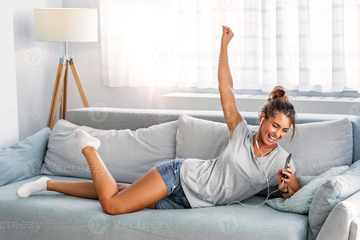 Happy young woman in earphones is listening to music with smart phone, dancing and smiling. Young woman listening to music online on smartphone in headphones photo