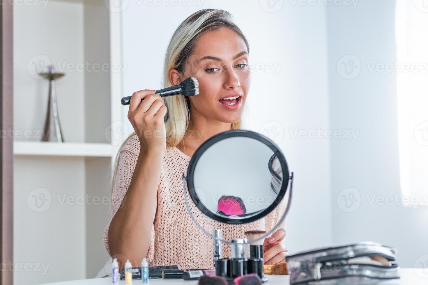 Beauty woman applying makeup. Beautiful girl looking in the mirror and applying cosmetic with a big brush. Girl gets blush on the cheekbones. Powder, rouge photo
