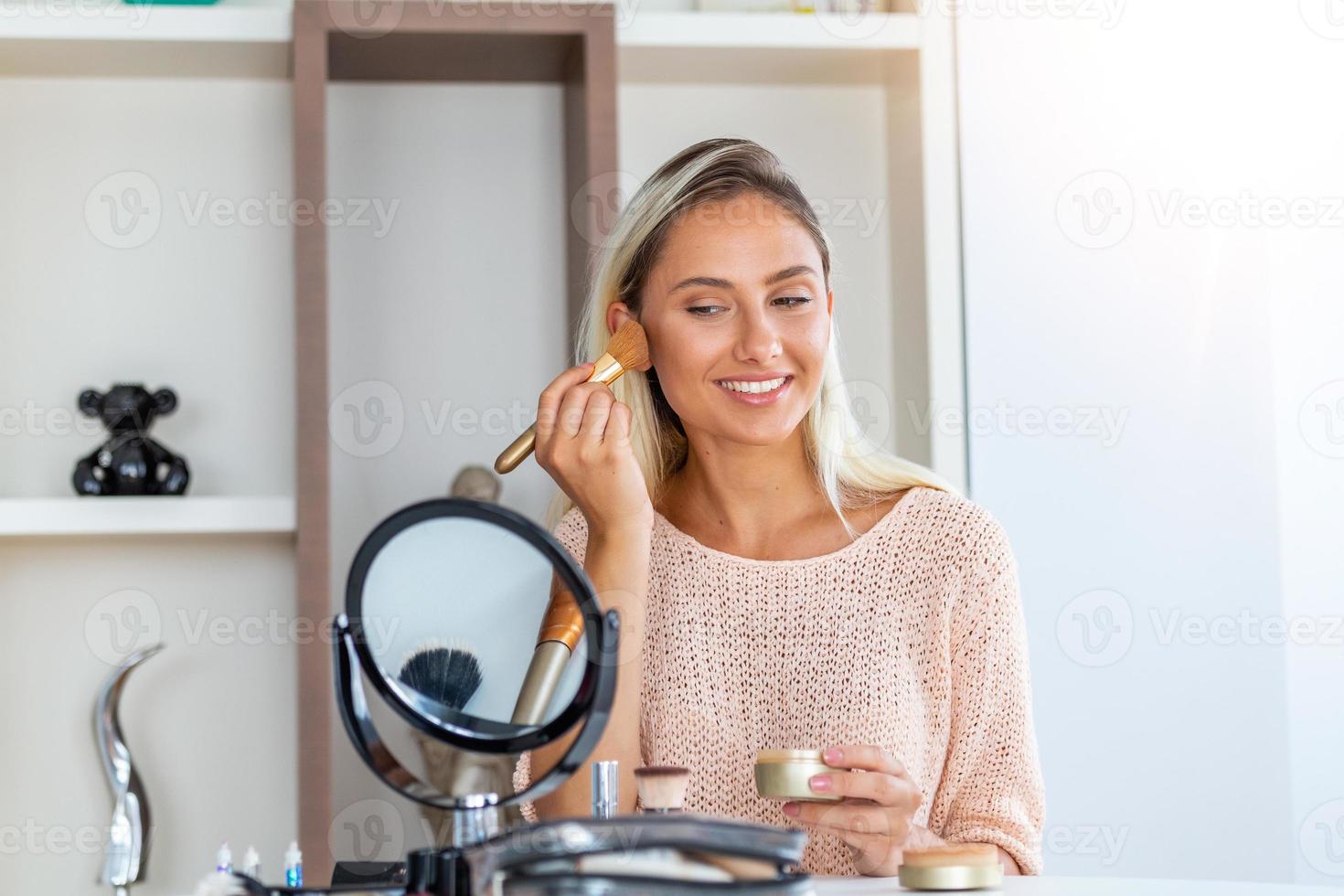 mujer de belleza al maquillarse. hermosa chica mirándose en el espejo y aplicando cosméticos con un cepillo grande. la chica se sonroja en los pómulos. polvo, colorete foto