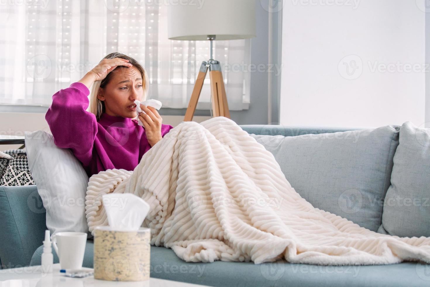 mujer enferma.gripe.mujer resfriada. estornudar en un pañuelo. dolor de cabeza. virus .medicamentos. mujer joven infectada con frío sonándose la nariz con un pañuelo. mujer enferma con dolor de cabeza sentada en un sofá foto