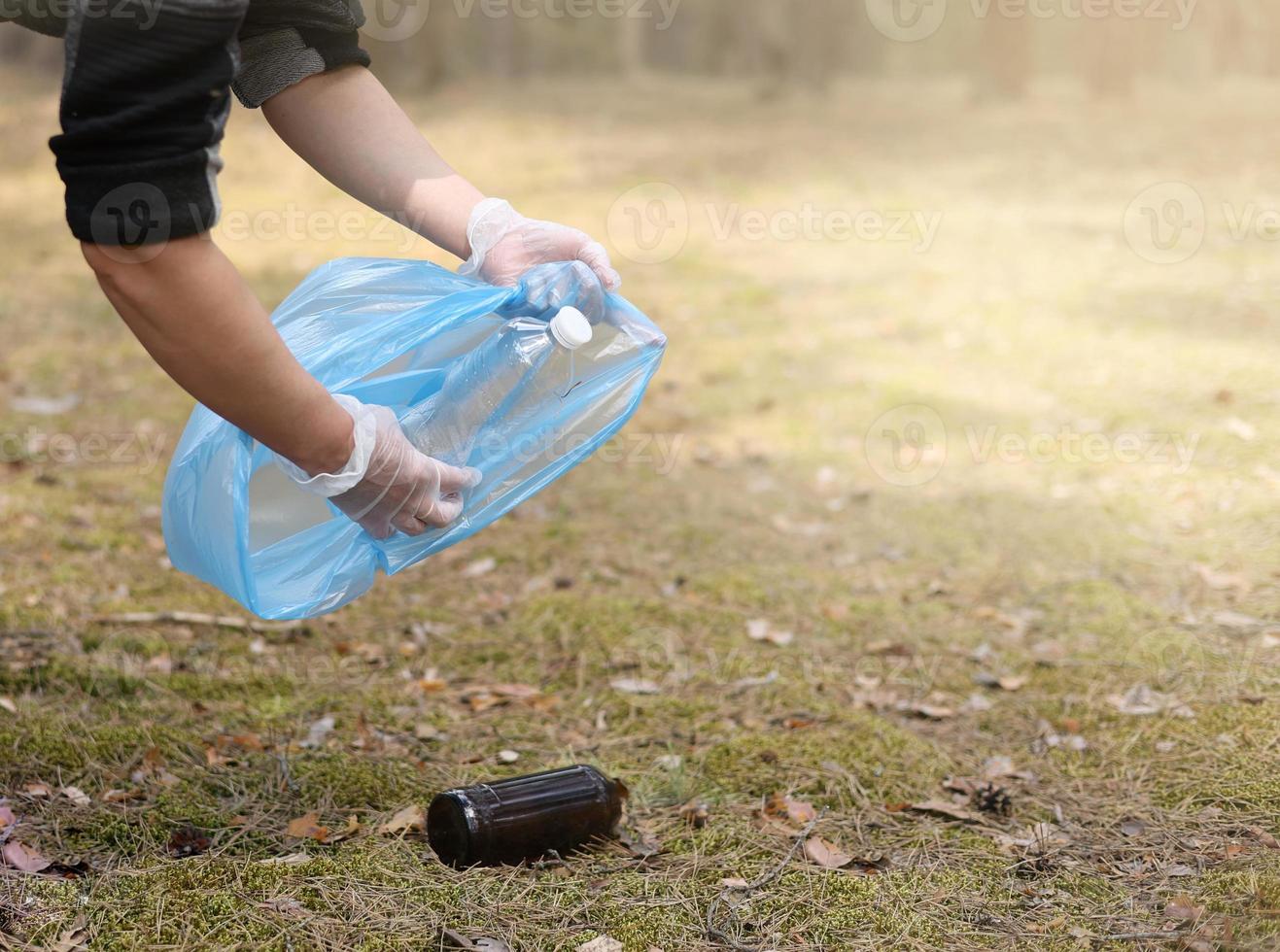 Young man collects trash plastic, glass from the ground. A volunteer cleans up the park on a sunny bright day. Clearing, pollution, ecology and plastic concept photo